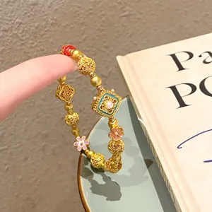 Gros plan du bracelet de perles en or de style ethnique chinois avec des fleurs en émail.