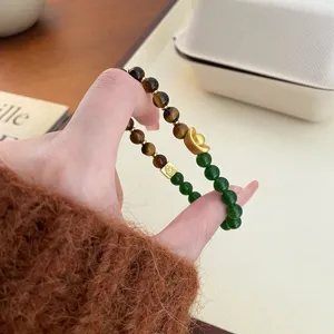 Vue rapprochée du bracelet en œil de tigre jaune et perles vertes avec pendentif lingot d'or.