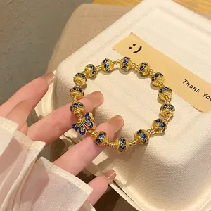Gros plan détail du bracelet de perles plaqué or vintage avec charm papillon en émail bleu.