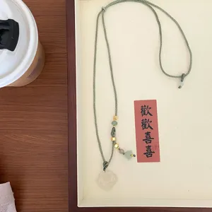 Detail view of a Chinese-style white agate necklace featuring green braided cord and gold beads.