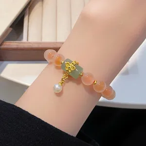 Gros plan détail du élégant bracelet de perles en agate avec cylindre de jade et charm doré.