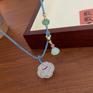 Detailed shot of Chinese retro white agate ruyi necklace with blue braided cord and gold beads.