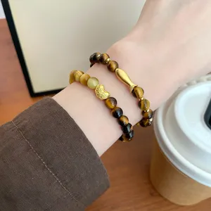 Nahaufnahme des natürlichen Tigerauge-Steinarmbands mit niedlichen Goldfisch- und Barren-Anhängern.
