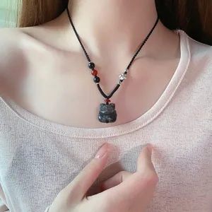 Gros plan d'un collier pendentif en obsidienne naturelle avec cordon tressé noir et perles.