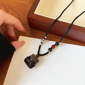 Vue détaillée du collier pendentif en obsidienne naturelle avec cordon tissé et perles rouges.