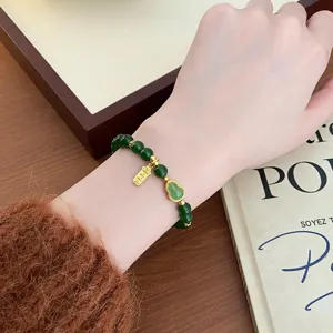Gros plan détaillé du bracelet de perles vertes de style chinois avec un pendentif gourde en or au poignet.