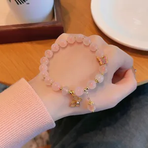 Gros plan détail du bracelet de perles d'agate rose douce avec de charmants papillons dorés.