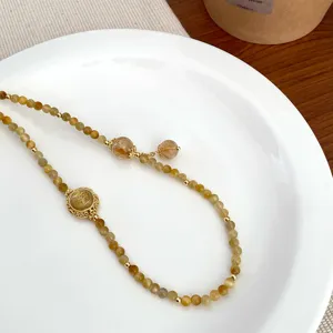 Detail shot of natural stone crystal beaded bracelet with exquisite gold metal charms on white plate.