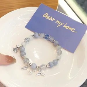 Close-up detail of blue beaded bracelet with cute whale tail and shell charms on plate.
