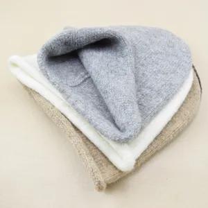Detailed closeup of stacked solid color knitted beanies in grey white and khaki cozy knit.