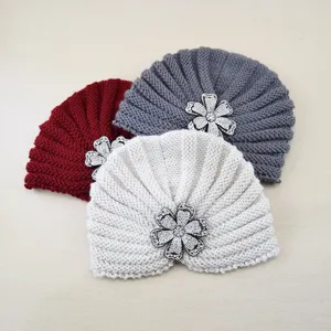 Detailed view of warm knitted turban hat with sparkling rhinestone flower brooch, cozy fabric.