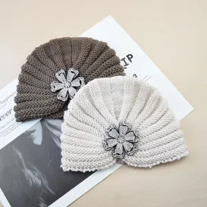 Detail shot of cozy knitted turban hats featuring sparkling rhinestone flower brooches in two colors.