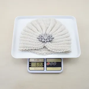 Vue détaillée du bonnet turban blanc en tricot avec décoration de broche fleur de cristal.