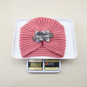 Detail shot of a pink knitted turban hat with rhinestone flower brooch, wool knit material.