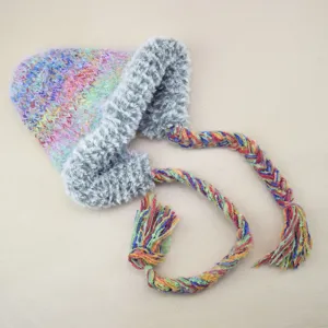 Nahaufnahme der bunten Strickmütze mit plüschigen Ohrenklappen und geflochtenen Quasten.