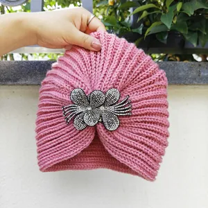 Close up of pink knit turban hat detail featuring sparkling rhinestone flower brooch accessory.