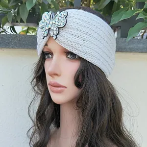 Weißes Strickstirnband mit glitzerndem Strass-Schmetterling, detailreiche Nahaufnahme.