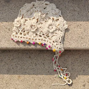 Close-up detail of beige crochet knit beanie cap with colorful wooden beads and tassels.