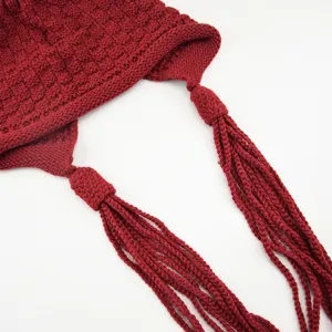 Dettaglio berretto in maglia rossa con motivo uncinetto quadrato e lunghe nappe trecciate.