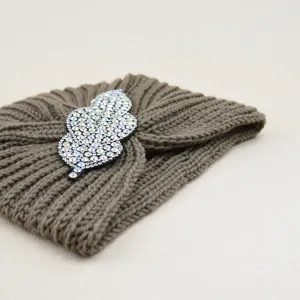 Close-up detail of knitted turban hat with sparkling rhinestone leaf brooch accessory.