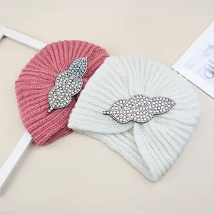 Detailed view of knitted turban hats with rhinestone leaf accessories, cozy winter headwear.