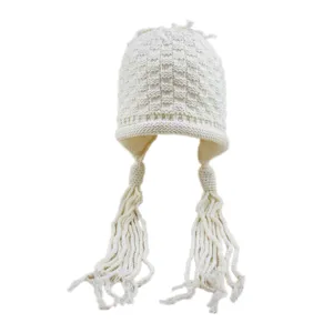 Vista dettagliata del berretto in maglia bianco sporco con motivo a quadri e nappe.