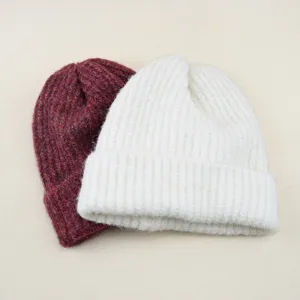 Close-up details of soft knit beanie hats in wine red and white, showing cozy winter texture.