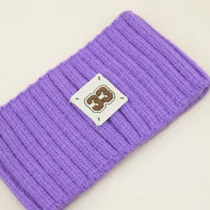 Primo piano dettagliato della fascia in maglia viola con coste verticali e toppa ricamata.