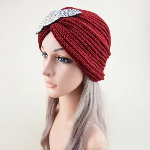 Detailed view of the red knit turban hat with rhinestone leaf accessory for winter warmth.