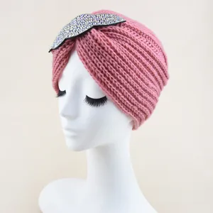 Detailed view of stylish pink knitted turban hat with sparkling rhinestone leaf accessory.