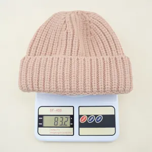 Detail view of a chunky knit kids beanie hat in soft pink, displayed on a scale showing weight.