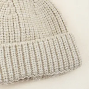 Close-up detail of cozy chunky knit baby beanie hat in soft beige color, ribbed texture.