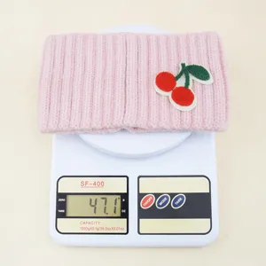 Dettaglio fascia per capelli rosa in maglia con ciliegia, morbido accessorio a coste con peso.