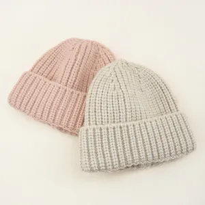 Detailed shot of cozy chunky knit children beanies in soft pink and beige colors for winter warmth.