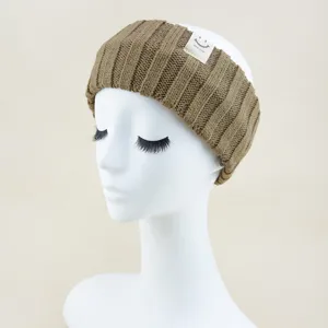 Close-up of brown knitted headband detail, featuring a cute smiley face woven label tag.