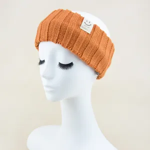 Details of the orange ribbed knit headband featuring a cute smiley face woven label accent.