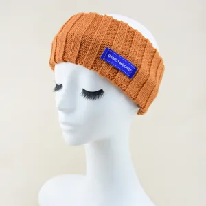 Gedetailleerd weergave van de oranje gebreide geribbelde haarband met blauw letterlabel voor yoga.
