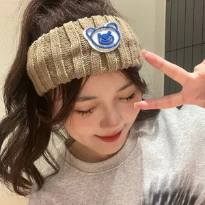 Detailed view of a knitted hair band with a cute blue bear patch, soft woolen wide headband.