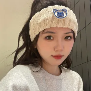 Detailed view of the cute beige knitted headband featuring a blue bear embroidery patch design.