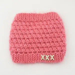 Dettaglio fascia in maglia rosa, soffice texture peluche, charm metallo X strass.