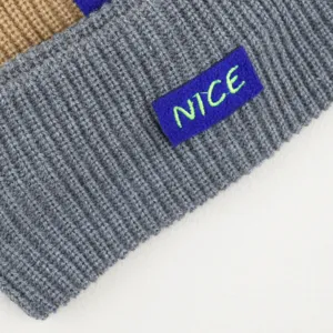 Close-up detail of knitted headband, grey winter ear warmer with embroidered NICE letter patch.