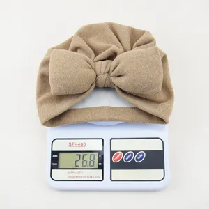 Detailaufnahme eines süßen Babyturbanhut in Khaki mit großer Schleife auf einer Digitalwaage.