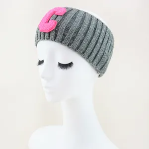 Dettaglio della fascia lavorata a maglia grigia con patch lettera C in ciniglia rosa.