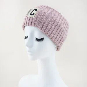 Gros plan détaillé d'un bandeau en tricot rose avec écusson de lettre et texture douce.