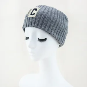 Gros plan sur le bandeau tricoté gris avec un écusson lettre C et une étiquette mode.