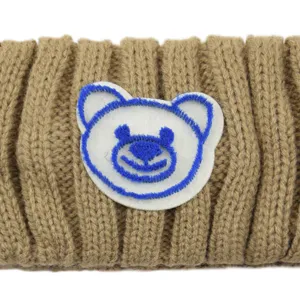 Detailed closeup of brown knitted hair band featuring a cute embroidered bear face patch.