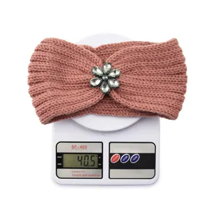 Detailed view of knitted headband with rhinestone flower ornament on scale showing weight.