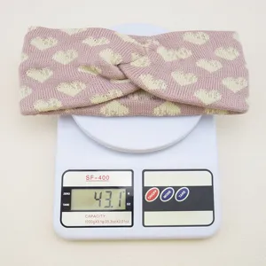 Detailansicht des rosa-gelben Herz-Jacquard-Strickstirnbandes auf einer Digitalwaage.
