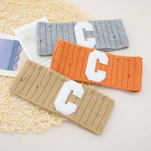 Detailed shot of knitted varsity letter C headbands in grey, orange, and khaki colors.