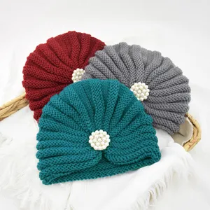 Detail shot of knitted turban hats with pearl flower decor in red, grey, and teal colors.